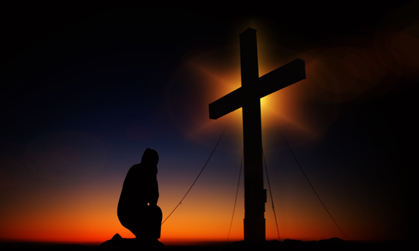 Ein Mann kniet in der Abenddämmerung vor einem Kreuz und betet.