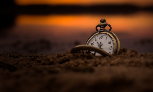 Abendstimmung am Meer mit Taschenuhr im Vordergrund, die 5 Minuten vor 12 anzeigt