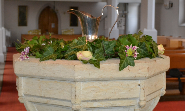 geschmückter Taufstein mit Taufkanne