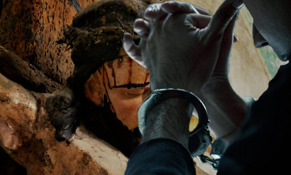 Betende Hände mit Handachellen im Vordergrund. Im Hintergrund Jesu blutendes Haupt am Kreuz.